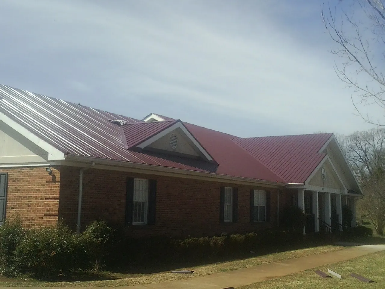 Red metal roof with gabled entries on a long brick building, from a Hail Damage Roof Repair job in Brookings