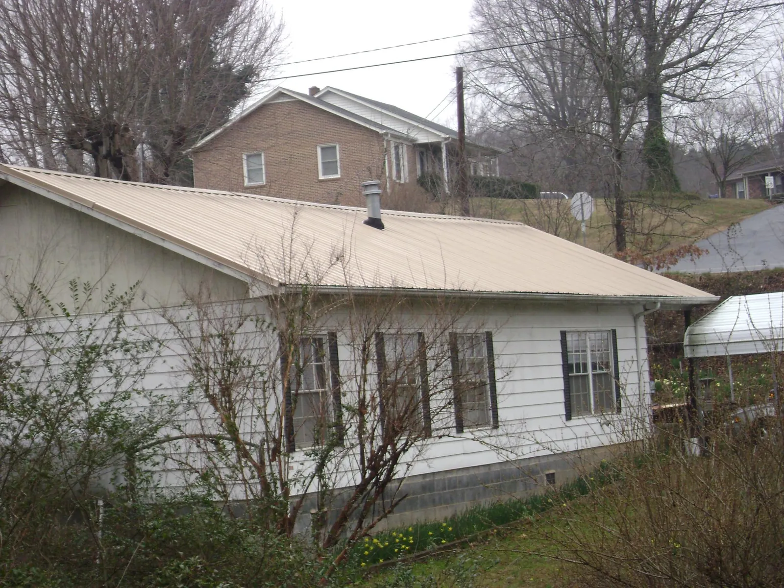Tan metal roof on a white sided house set into a hillside — Commercial Roofing by Roofing Brothers in Brookings